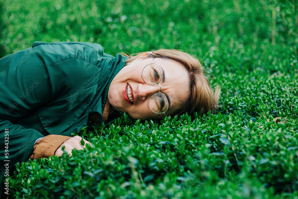 Stylish woman in glasses and green coat lying on green bushes Stylish woman in glasses and green coat lying on green bushes