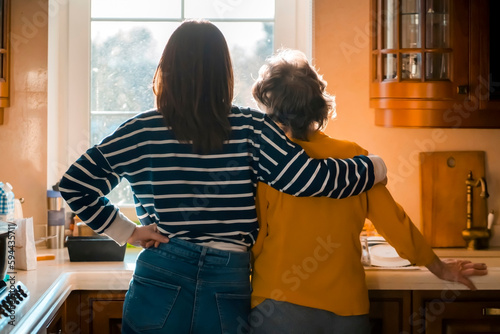 Daughter and her old mother stands near the window and hugs.