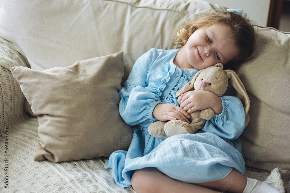 Cute little girl in blue dress on the sofa at home with her favourite ...