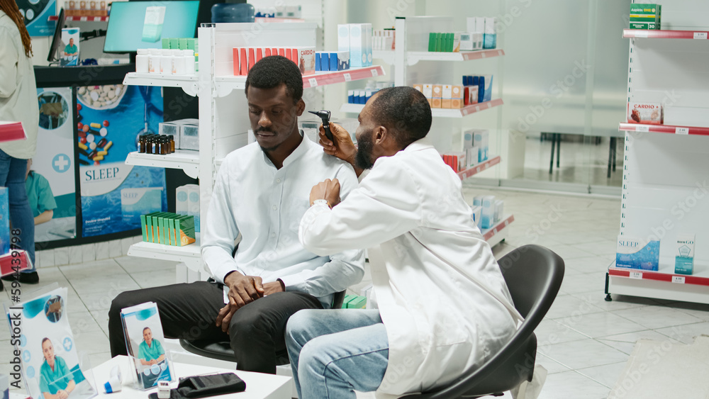 Obraz premium Health specialist consulting client with otoscope at clinic, sitting in pharmacy and doing ear examination. Young otologist and customer checking infection for otolaryngology consultation.