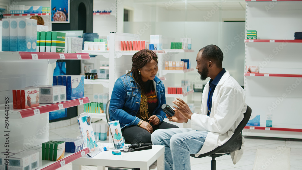 Fototapeta premium African american doctor giving bottle of pills to woman, explaining about prescription medicine and sickness cure. Male pharmacist talking about vitamins and supplements, drugs packages.