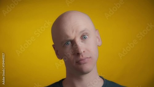 Man with blue eyes and bright skin looking straight towards the camera and raises one eyebrow and tilts his head on a yellow background, Real time. photo
