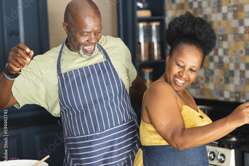 Happy senior african american couple wearing aprons and dancing in kitchen