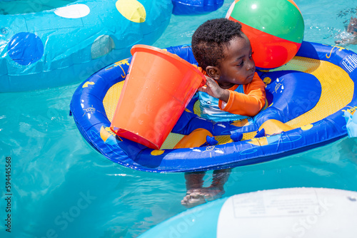 Young boy on a float playing with a bucket in an outdoor swimming pool