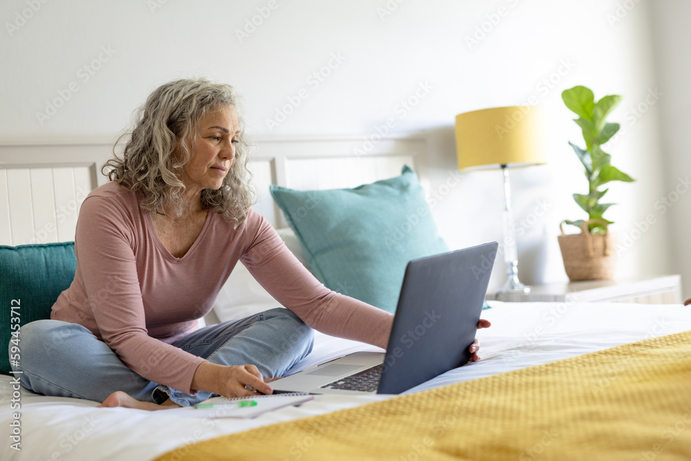 Happy senior caucasian woman sitting on bed and using laptop Happy senior caucasian woman sitting on bed and using laptop