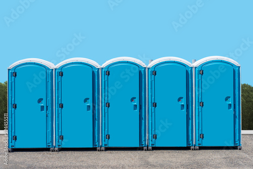 Tableau sur toile A group of outdoor portable outhouse public toilets with a blue background