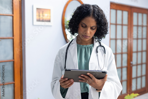 Biracial female doctor wearing sthethoscope, using tablet at doctor's office