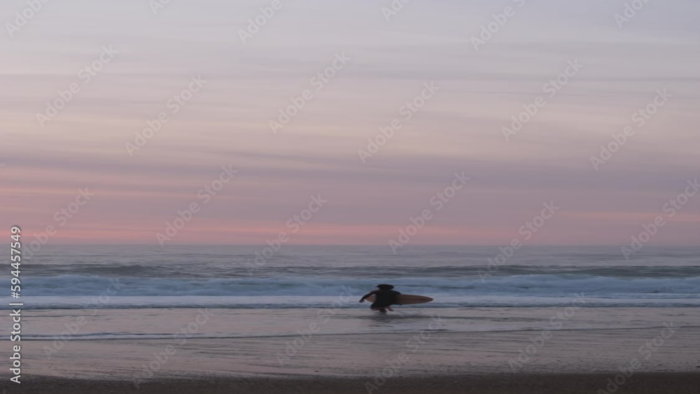 vertical video of a surfer entering the water in a beautiful sunset with pink and white colors