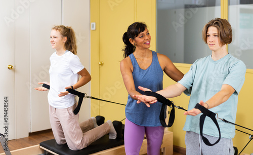 Pilates instructor helping teen boy and girl do hand stretch on the machine in the gym