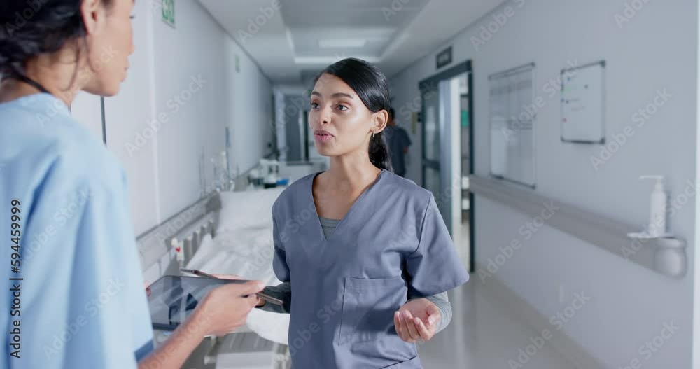 Diverse doctor and nurse using tablets and talking in corridor at hospital, in slow motion Diverse doctor and nurse using tablets and talking in corridor at hospital, in slow motion