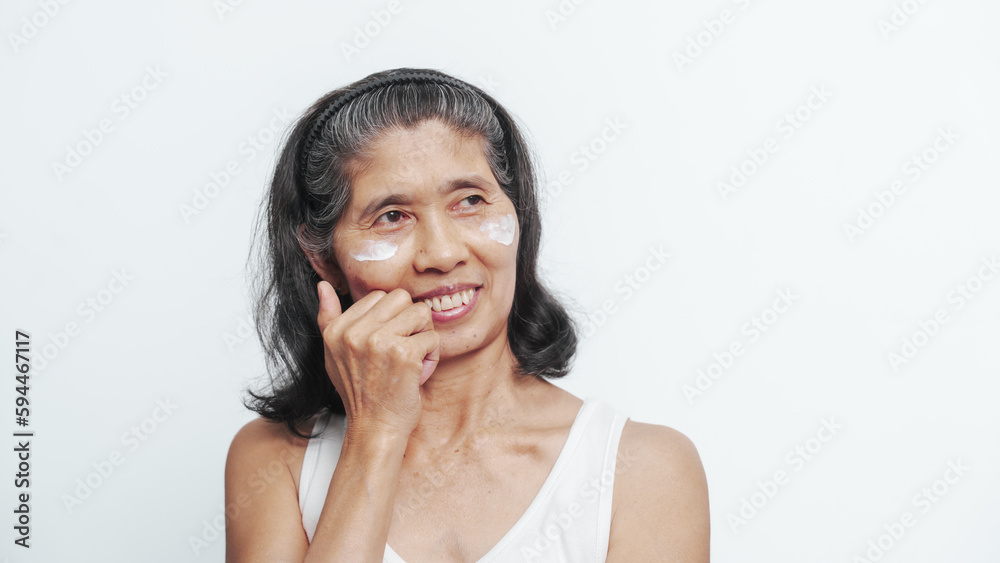 Close up face of female elderly mature older asian chinese housewife applies anti aging facial cream on face, old skincare treatment Close up face of female elderly mature older asian chinese housewife applies anti aging facial cream on face, old skincare treatment