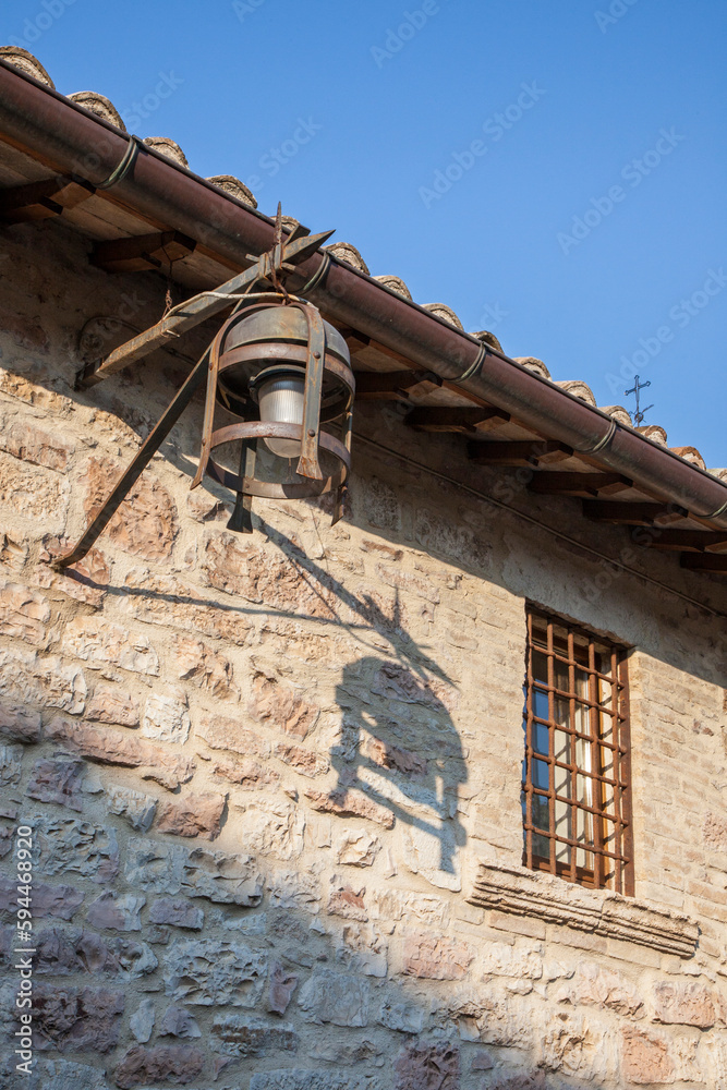 Italy, Umbria. Street lamp and shadow on a stone wall along the streets of Assisi.