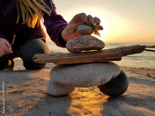 A young girl puts the final rock on an inuksuk inukshuk she's built at the beach at sunset 2 photo