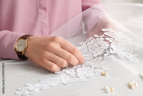 Dressmaker working with beautiful white lace at table in atelier, closeup