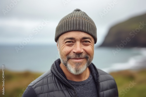 Group portrait photography of a grinning man in his 40s wearing a warm beanie or knit hat against a summer landscape or beach background. Generative AI