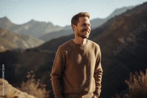 Handsome young man in casual clothes standing on the top of a mountain and looking away
