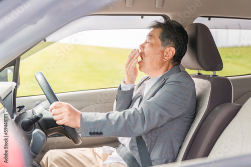 自動車の運転中に眠気を感じてあくびをする高齢者・シニア男性
 photo