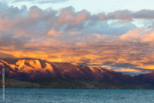 Gazing at the high-altitude lake Manasarovar at sunset in Tibet is a stunning experience. The sun's rays pierce through the clouds, casting a warm glow on the serene and smooth surface of the lake. photo