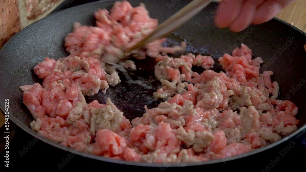 Spaghetti, close-up of frying ground meat on a pan, which is being stirred with a wooden spoo Spaghetti, close-up of frying ground meat on a pan, which is being stirred with a wooden spoo