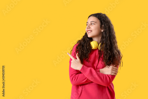 Teenage girl with headphones pointing at something on yellow background