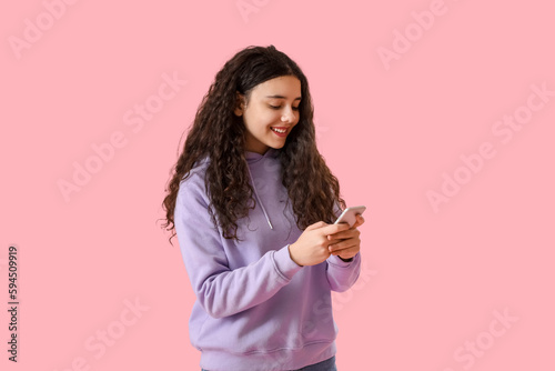 Teenage girl in hoodie using mobile phone on pink background