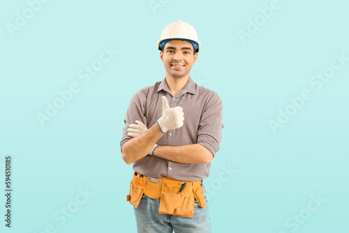 Young carpenter in hardhat showing thumb-up on blue background