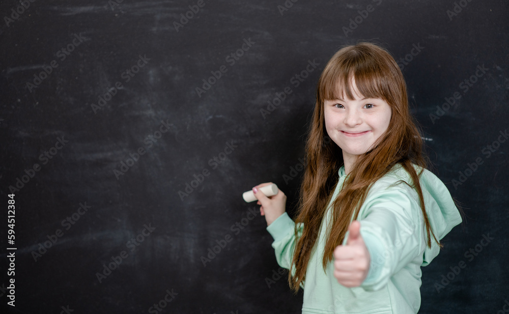 Smiling young girl with Downs syndrom wants to write something on the chalkboard. Empty space for text