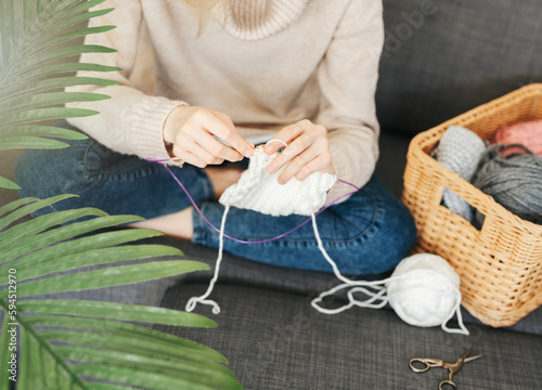 Young woman knitting warm scarf indoors