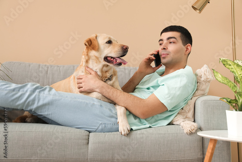 Young man with his Labrador dog talking by mobile phone on sofa at home
