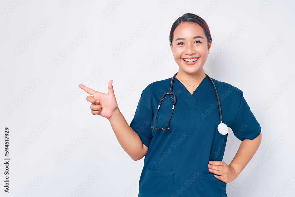 Smiling young Asian female professional nurse working wearing a blue uniform standing confident while pointing finger at empty copy space isolated on white background. Healthcare medicine concept Smiling young Asian female professional nurse working wearing a blue uniform standing confident while pointing finger at empty copy space isolated on white background. Healthcare medicine concept