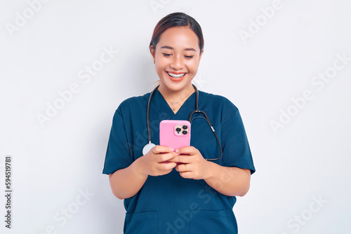 Smiling friendly young Asian woman nurse working wearing a blue uniform using a mobile phone on messaging or using an app isolated on white background. Healthcare medicine concept