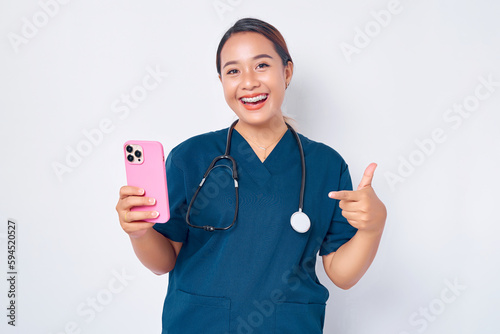 Cheerful young Asian woman professional nurse working wearing a blue uniform holding mobile phone and showing thumb up gesture isolated on white background. Healthcare medicine concept