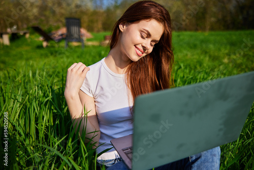 happy, joyful woman working on a laptop while sitting in a field photo