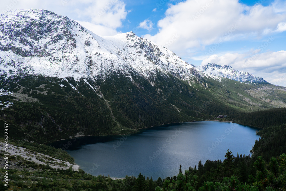 Morskie Oko Snowy Mountain Hut in Polish Tatry mountains, drone view, Zakopane, Poland. Aerial view shot of beautiful green hills and mountains in dark clouds and reflection on the lake Morskie Oko