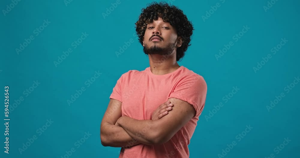 Portrait of handsome serious young Indian man in t-shirt standing over blue studio background Portrait of handsome serious young Indian man in t-shirt standing over blue studio background
