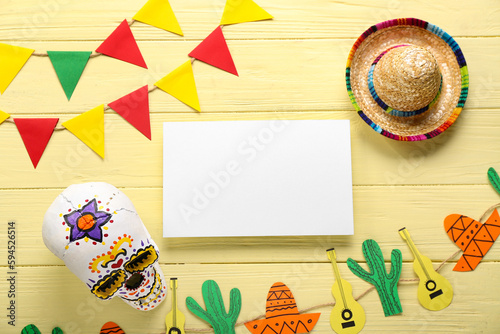 Blank card with painted skull, sombrero hat and Mexican flags on yellow wooden background