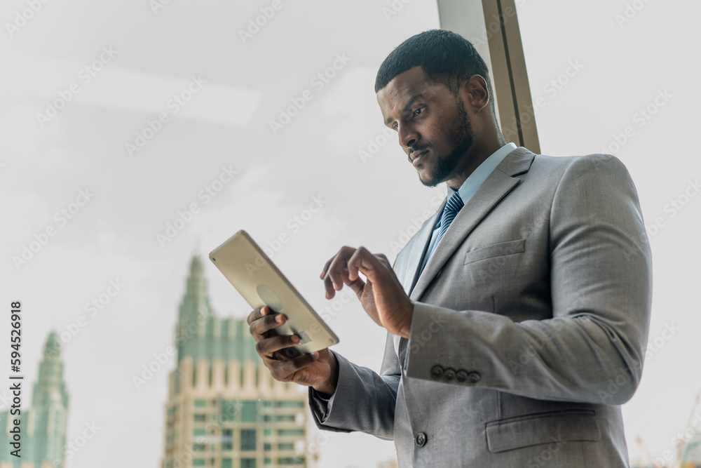 Handsome black businessman with a digital tablet over a glass window overlooking the city skyline Handsome black businessman with a digital tablet over a glass window overlooking the city skyline