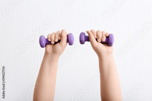 Woman with dumbbells near white wall, closeup