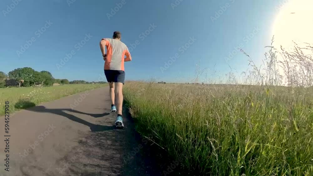 Fast approach through vegetation of a male trail runner on floodplains valley dyke bike path. Athlete endurance training run exercise outdoor sports concept. Fast approach through vegetation of a male trail runner on floodplains valley dyke bike path. Athlete endurance training run exercise outdoor sports concept.