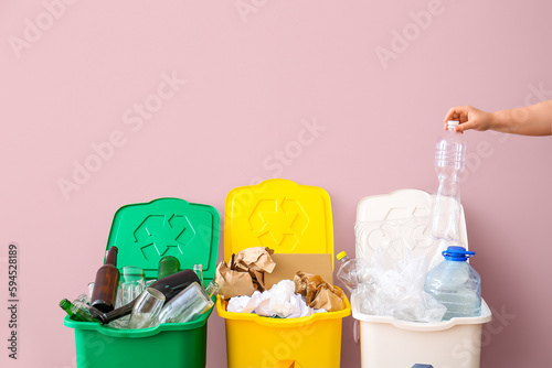 Woman throwing garbage into trash bin near pink wall. Recycling concept
