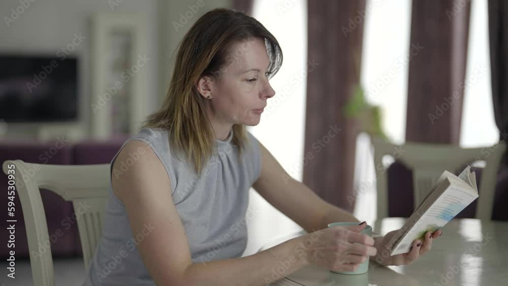 middle-aged woman spending weekend at home, relax and reading book in living room, drinking coffee middle-aged woman spending weekend at home, relax and reading book in living room, drinking coffee