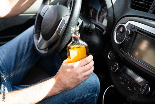 Driver driving a car with a bottle of alcohol in his hands close-up. © vfhnb12