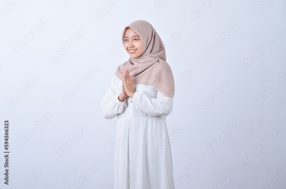 Beautiful Asian woman in white gamis and hijab smiling cheerfully showing namaste gesture isolated in white background Beautiful Asian woman in white gamis and hijab smiling cheerfully showing namaste gesture isolated in white background