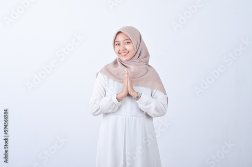 Beautiful Asian woman in white gamis and hijab smiling cheerfully showing namaste gesture isolated in white background