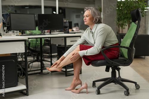 Caucasian woman massaging her tired legs while sitting in the office. 
