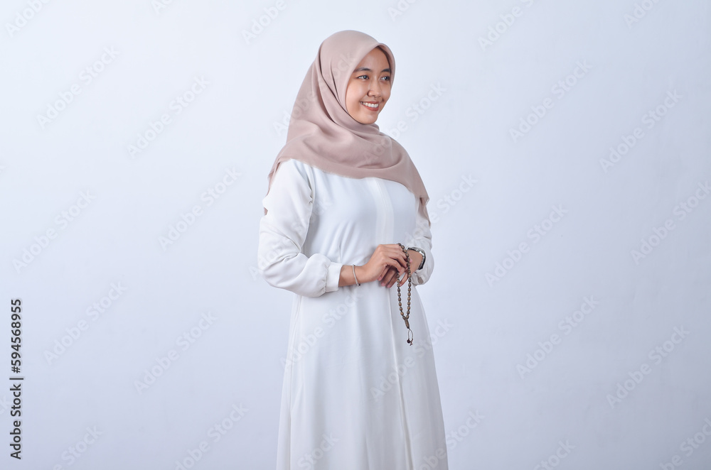 Beautiful Asian woman in white gamis and hijab smiling cheerfully buring prayer beads isolated in white background Beautiful Asian woman in white gamis and hijab smiling cheerfully buring prayer beads isolated in white background