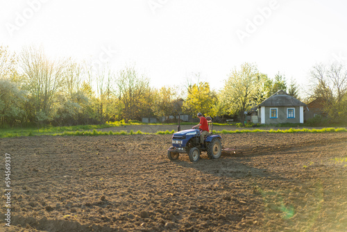 The tractor drives across the field and cultivates the land. Agricultural vehicle works in countryside. Sowing is the process of planting seeds in the ground as part of the early spring time