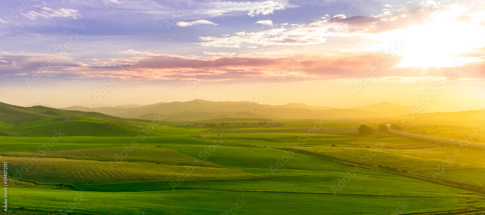 countryside sunset in green hills of spring fields with old castle farm and mountains on background of evening landscape