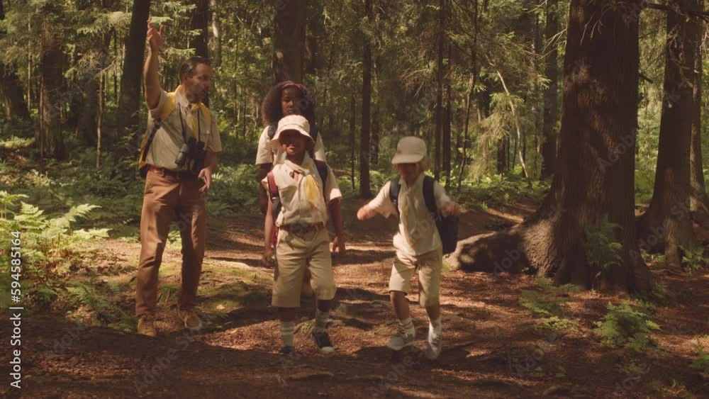 Multiethnic group of children in scout uniform and their leader hiking in forest together on sunny day exploring area Multiethnic group of children in scout uniform and their leader hiking in forest together on sunny day exploring area