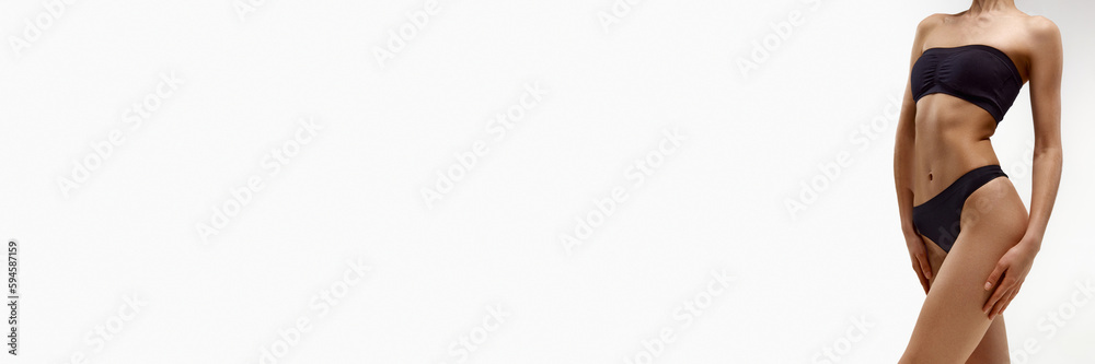 Obraz premium Cropped image of beautiful, slim, fit, tanned female body in black underwear against white studio background. Concept of beauty, body care, fitness, spa, health, figure. Banner. Copy space for ad
